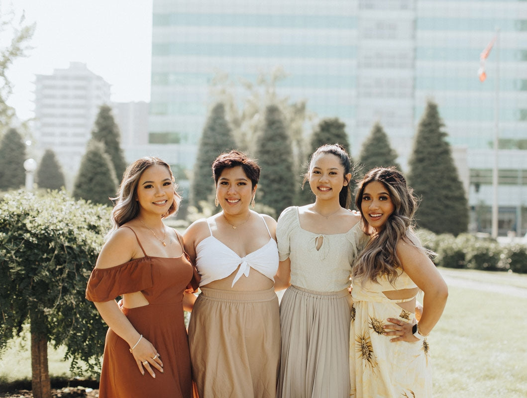 four ladies wearing sundresses posing for a photo with pine trees in the back and an all-glass building